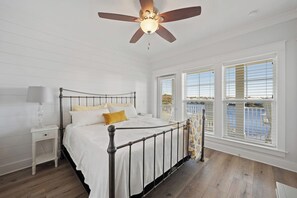 A bedroom with a bed, a nightstand, a ceiling fan, and large windows. - Modern House with Pool Access (Panama City Beach)