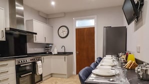 A modern kitchen with white cabinets, a black stove, and a dining area with a long table set for breakfast. - 7-bed Beachside Retreat - Sleeps 14 & Pet Friendly (Blackpool)