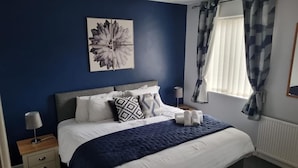 A bedroom with a bed, bedside tables, a window with curtains, and a wall-mounted artwork. - 7-bed Beachside Retreat - Sleeps 14 & Pet Friendly (Blackpool)