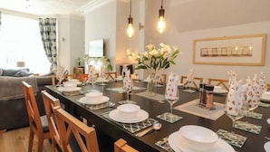 A dining area with a long table set for a meal, chairs, and a vase with flowers. - 7-bed Beachside Retreat - Sleeps 14 & Pet Friendly (Blackpool)