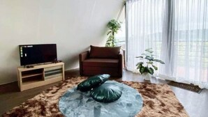 A living room with a flat-screen TV, a brown sofa, a large furry rug, and a potted plant. - Viewscape Nature Park Tanay powered by Cocotel (Tanay)