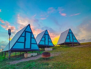 Drie puntige tenten met zonnepanelen, gelegen op een grasveld met een ondergaande zon.