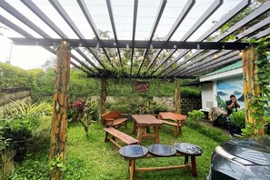 Un'area salotto esterna coperta con tavoli e panche in legno, immersa nel verde e decorata da un murale.