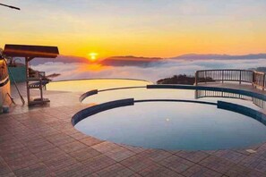 Una piscina circolare con vista sul tramonto, un pontile di legno e una ringhiera metallica.
