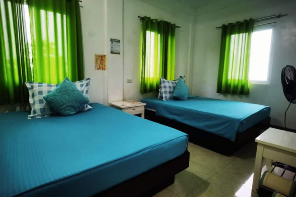 A room with two beds, each with a blue bedspread and a pillow. There is a small table and a chair in the corner.