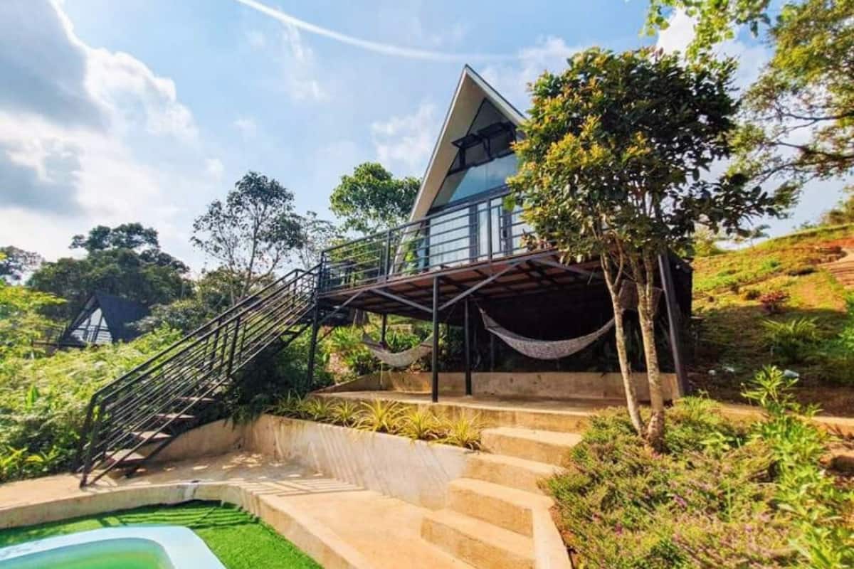 A modern villa with a triangular roof, a staircase leading to a balcony, and a pool area.