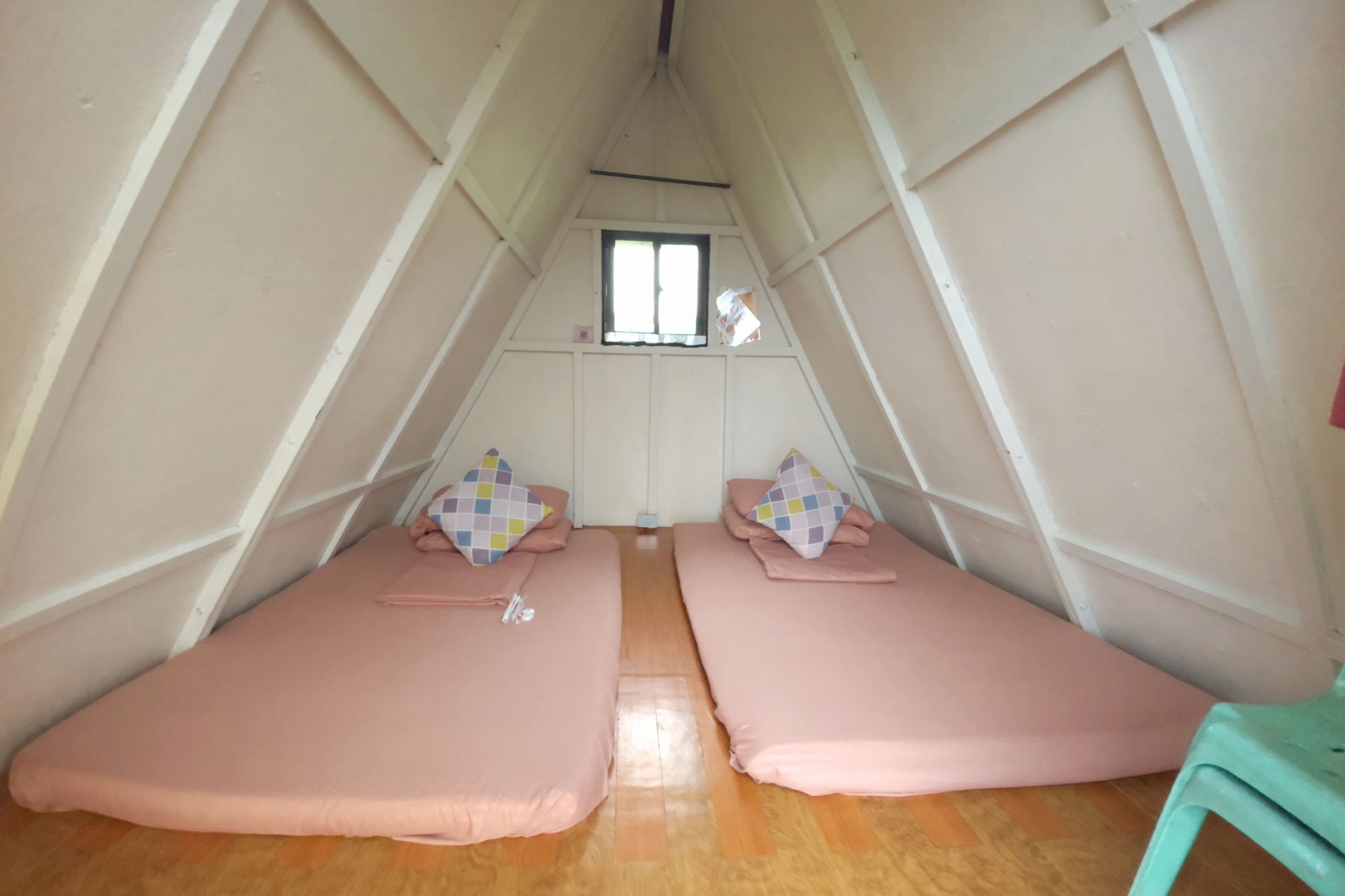 A triangular room with two beds, a window, and a wooden floor.