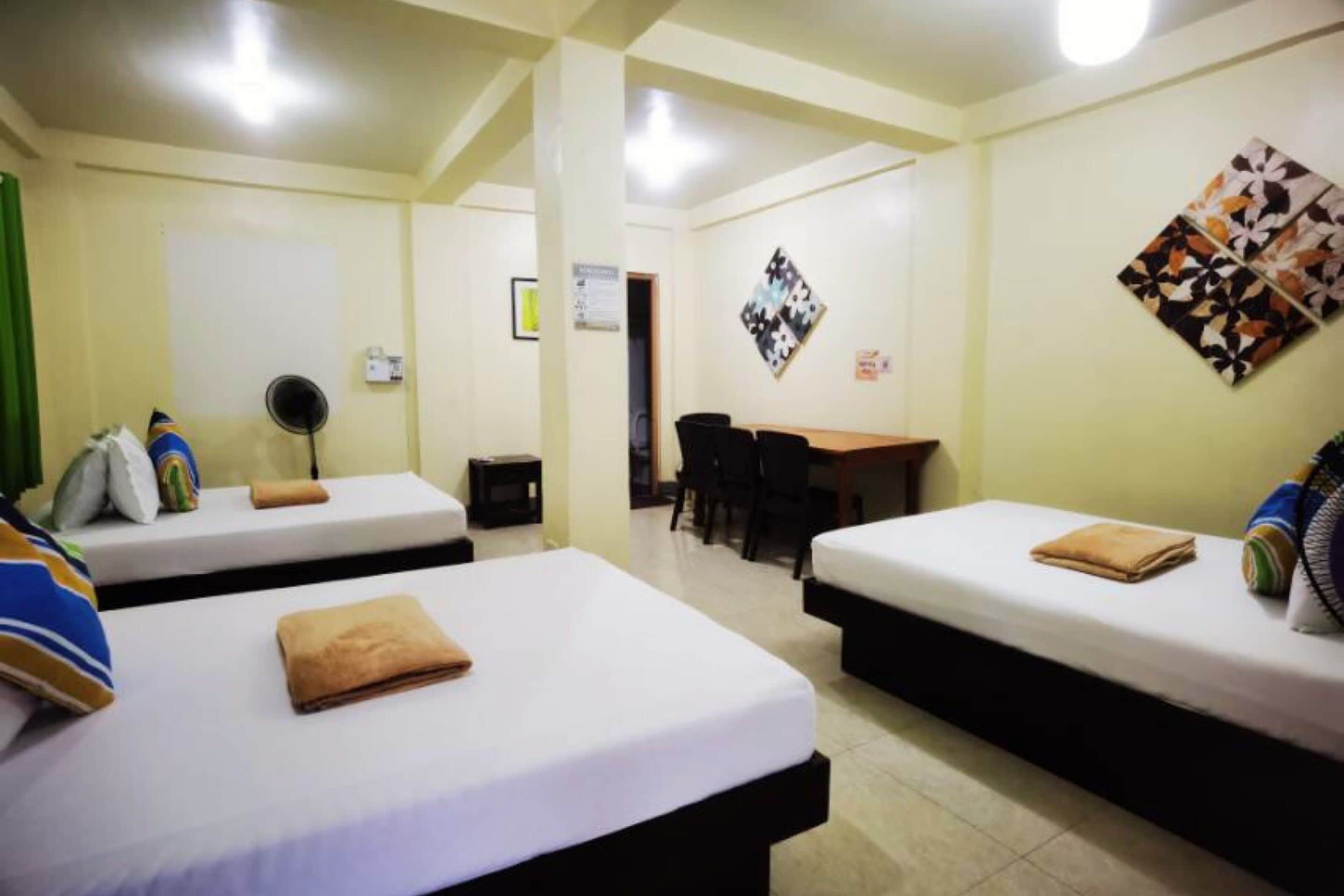 A hotel room with two beds, a desk, and a chair. There are pillows and a folded towel on each bed.