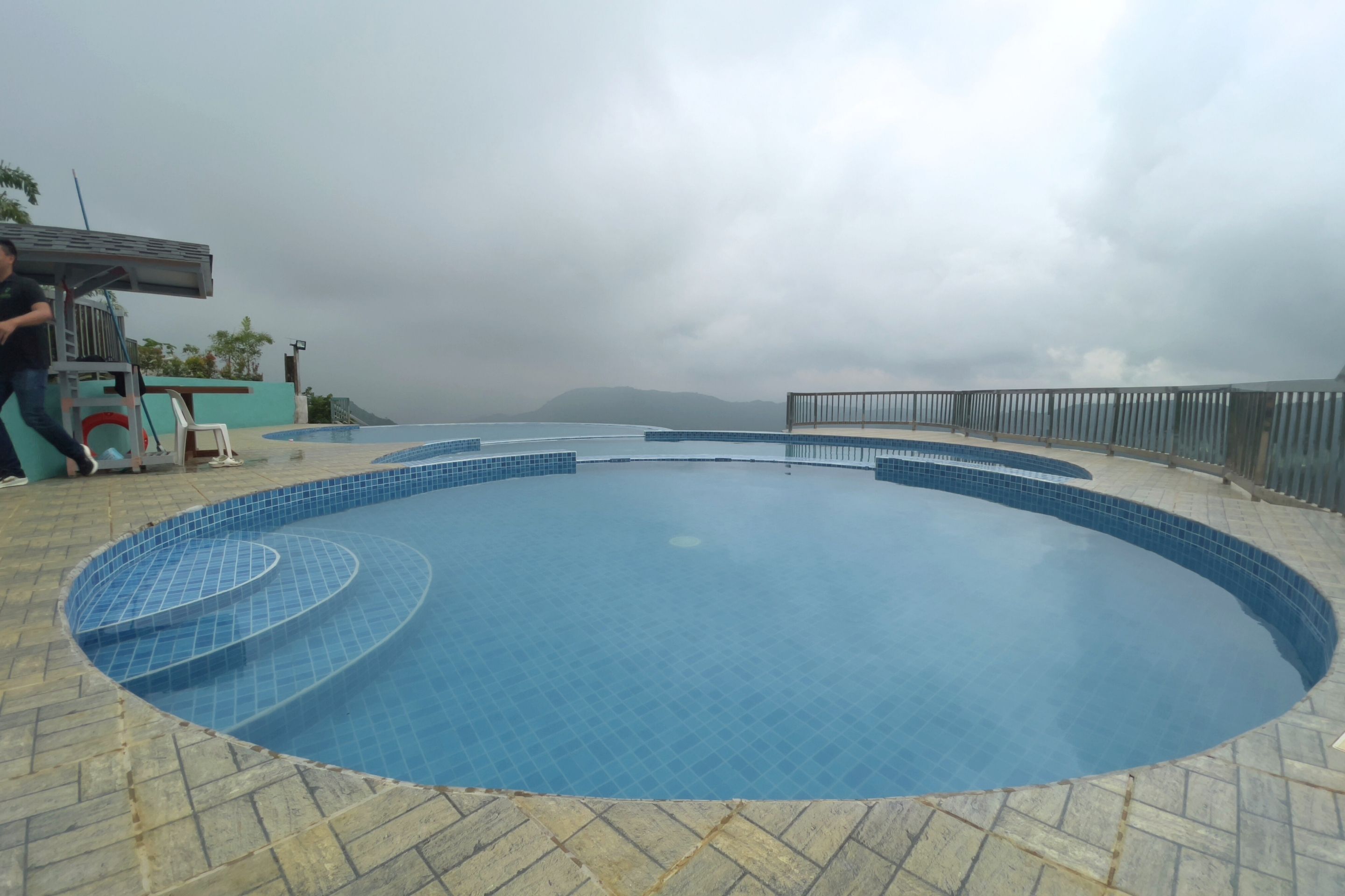 A swimming pool with a tiled edge, a covered area with a ladder, and a view of distant mountains.