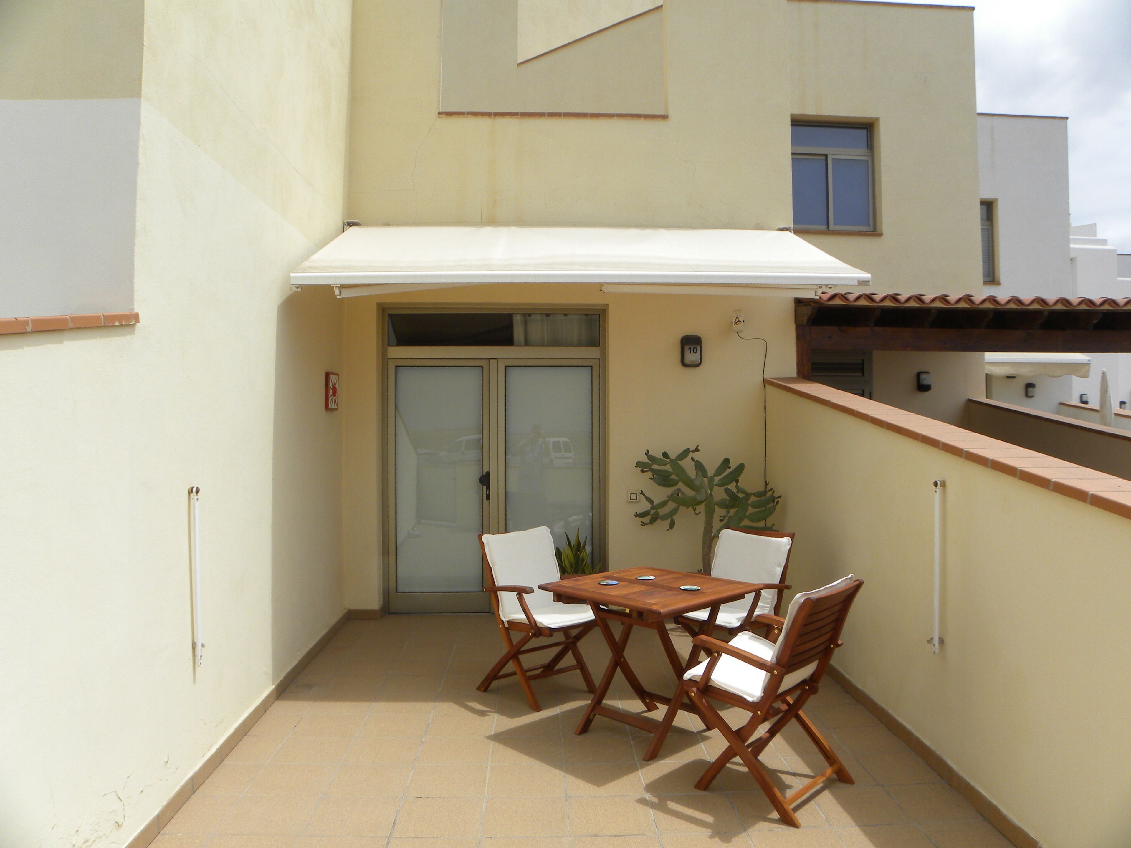 A small outdoor patio with a table and four chairs, a sliding glass door, and a small potted plant.