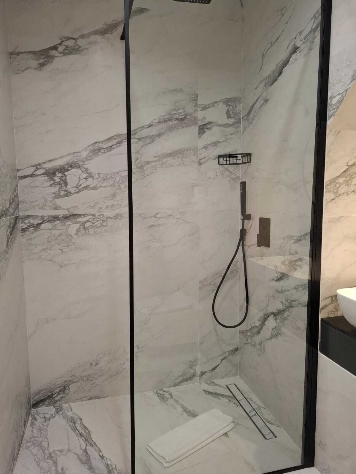 Eine moderne Dusche mit Glastrennwand, Marmorwänden und einer Handbrause.
