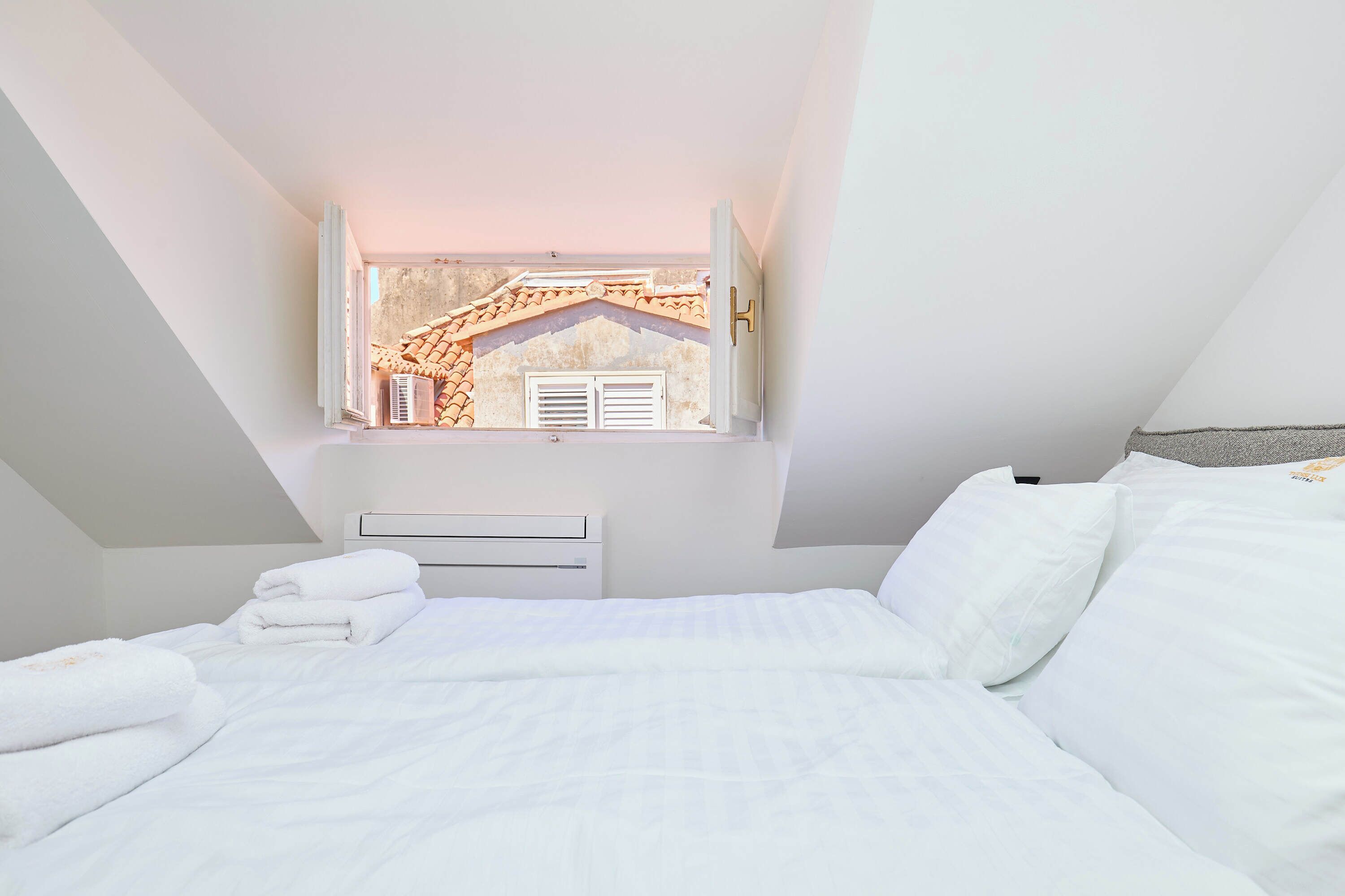 A bedroom with a sloped ceiling, a bed with white linens, and a wall-mounted air conditioning unit.