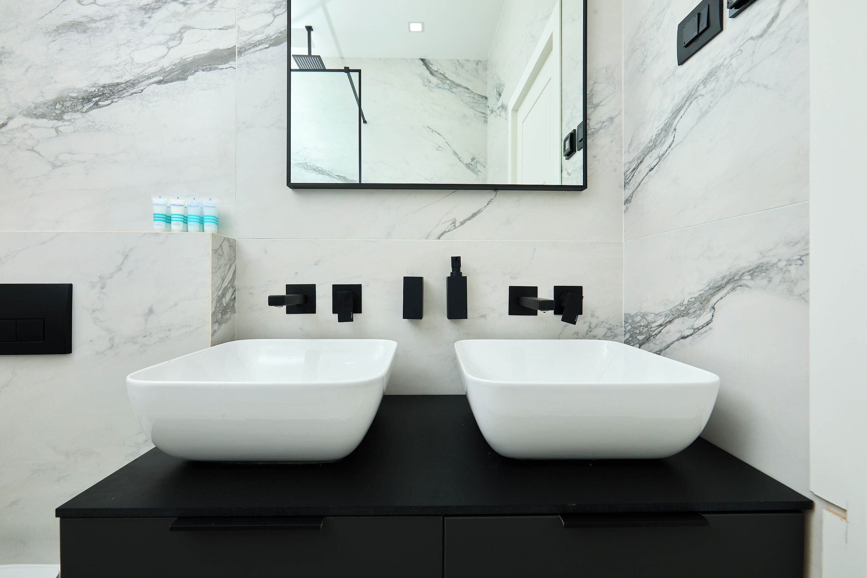 A modern bathroom with two white vessel sinks, black faucets, and a large mirror above the sinks.