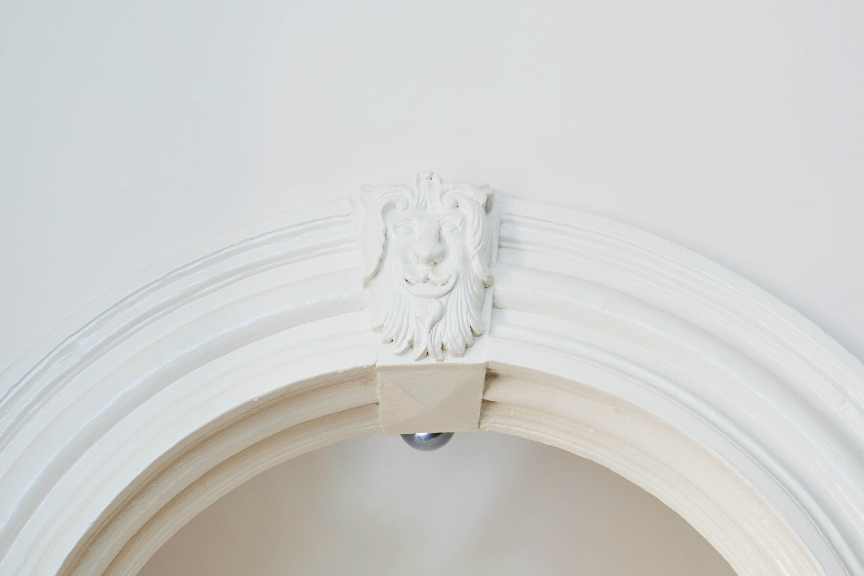 A white, ornate wall with a decorative lion head emblem.