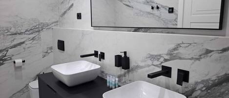 Un baño moderno con dos lavamanos blancos, dispensadores de toallas negros y un espejo grande arriba.