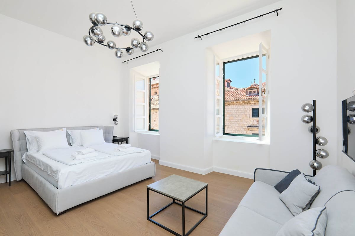 A modern bedroom with a bed, a sofa, a small table, and a chandelier.