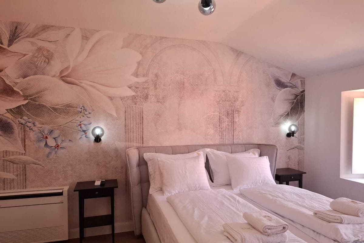 A bedroom with a large floral mural on the wall, a bed with white linens, two bedside tables, and a window with daylight.