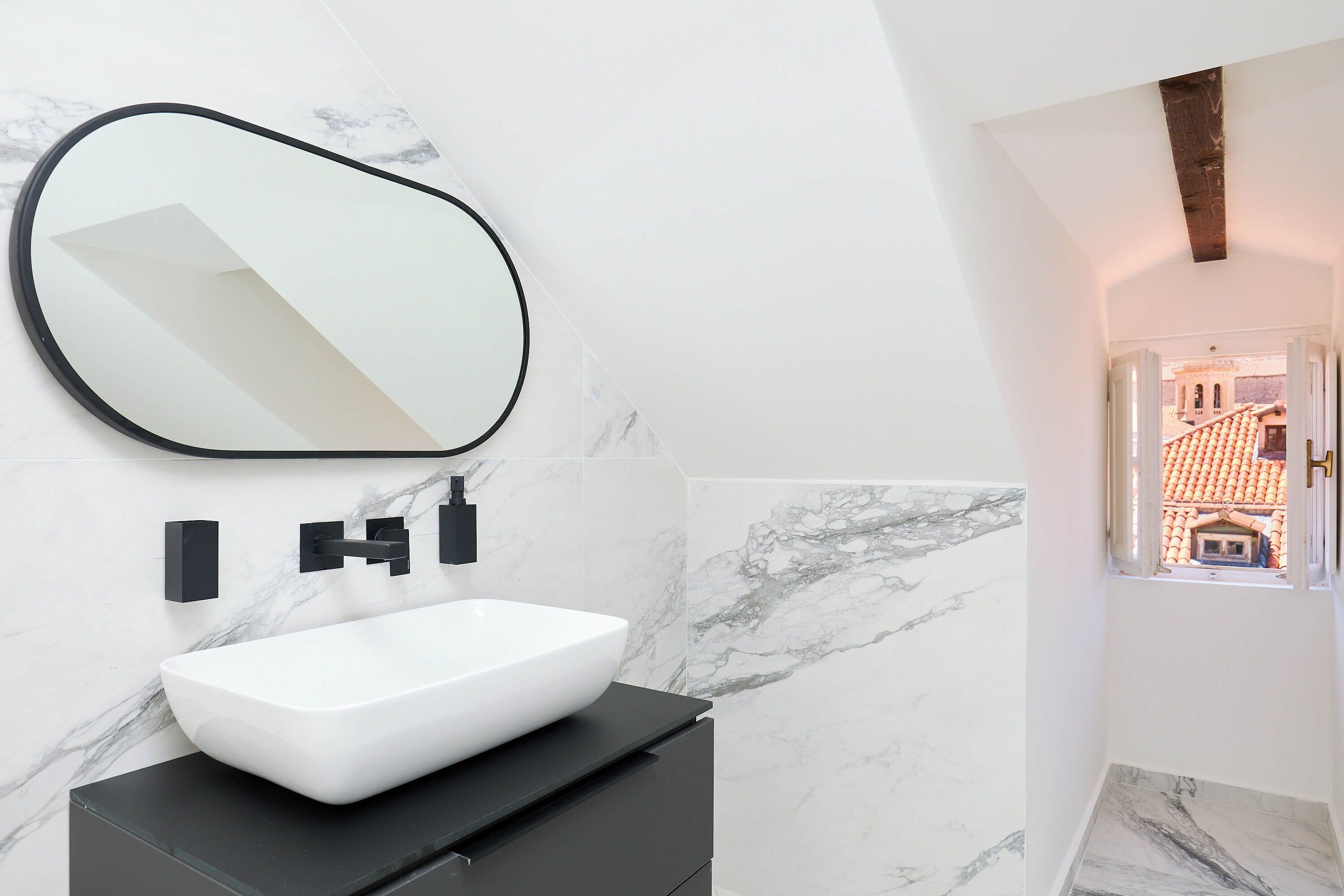 Un baño moderno con un lavabo de diseño blanco, encimera negra y un espejo grande.