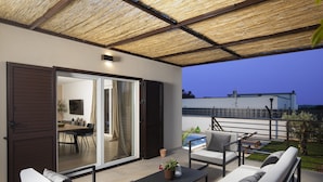 Un área de estar al aire libre techada con piscina, puertas corredizas y vista a un edificio en el fondo.