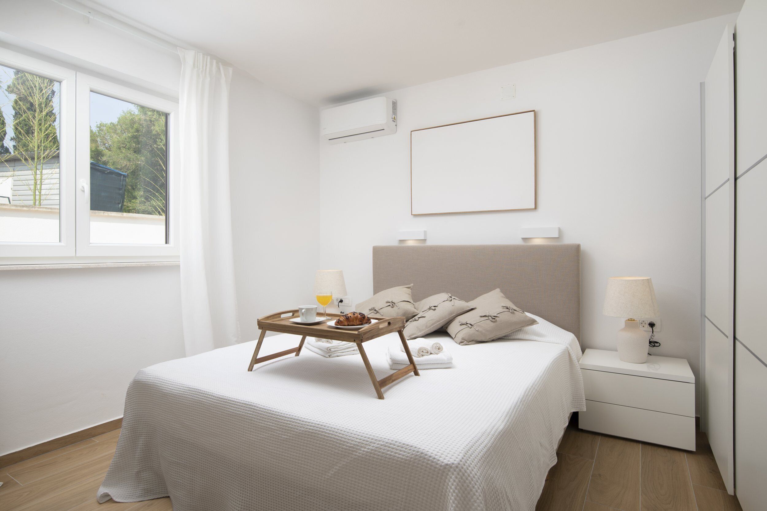 Een keurig opgemaakt slaapkamer met een bed, nachtkastjes, een bedlampje en een raam met gordijnen.