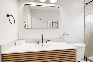 Un baño moderno con un espejo grande, un lavabo blanco y un mueble de tocador de madera.