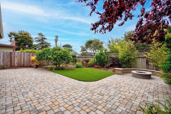 A backyard with a paved patio, a small lawn, and a fire pit.