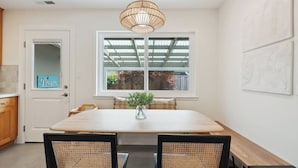 Una cocina con una mesa de madera, dos sillas, una lámpara colgante y una ventana con vistas a un jardín.