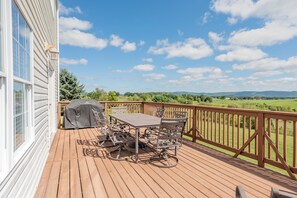 Une terrasse en bois avec une table et des chaises, un barbecue et une vue sur un paysage verdoyant.