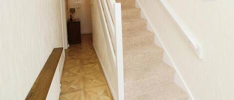 A hallway with a carpeted floor, a wooden bench, and a staircase with beige carpeted steps.