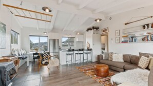 Amplia sala de estar con sofá, mesa de centro y chimenea. Zona de cocina con mesa y sillas.