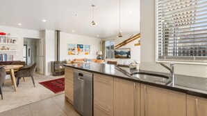 A modern kitchen with a central island, stainless steel appliances, and a dining area with a red rug. - Amazing Location! Central 2 bedroom Unit (Wānaka)