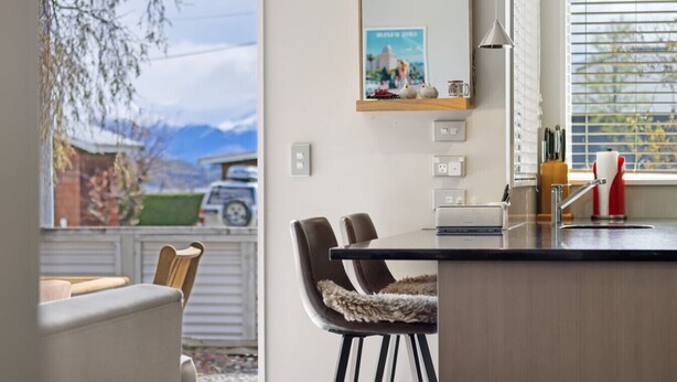 A modern kitchen with a dining area, a large window with a view of mountains, and a mounted mirror above the counter. - Amazing Location! Central 2 bedroom Unit (Wānaka)
