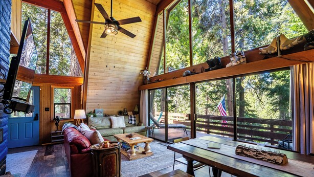 L’intérieur d’un chalet accueillant, avec un plafond en bois, de grandes fenêtres, un canapé, une table basse et une table à manger.