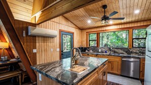 L’intérieur d’une cabane en bois comprend une cuisine dotée d’un comptoir en granit, d’appareils électroménagers en acier inoxydable et de grandes fenêtres.