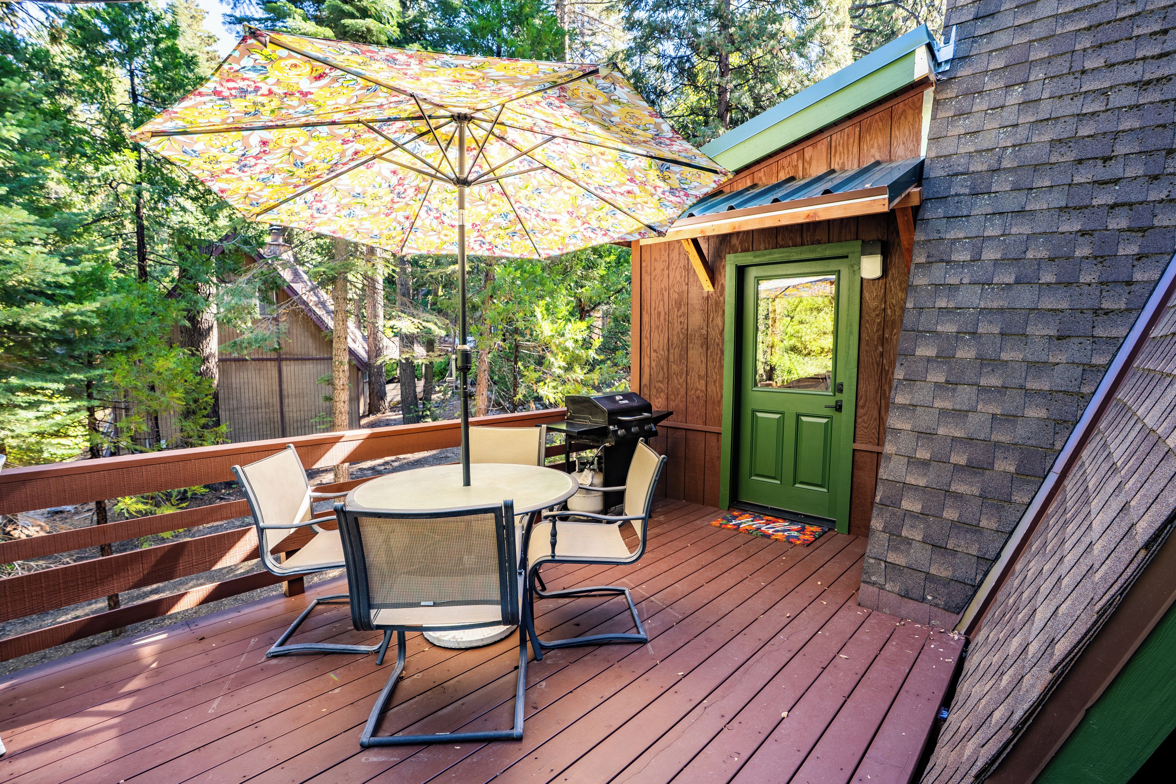Een houten terras met een tafel, stoelen, een barbecue en een groene deur.