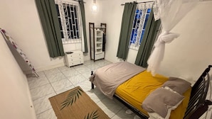 A bedroom with a bed, a bedside table, a wardrobe, and a window with curtains. - Tropical Paradise Retreat in Soufriere (Soufriere)