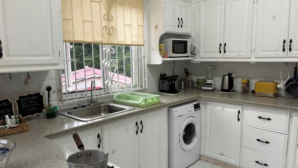 A kitchen with white cabinets, a microwave, a washing machine, and a gas stove. - Tropical Paradise Retreat in Soufriere (Soufriere)