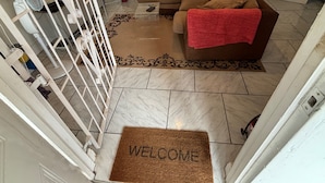 A living room with a brown sofa, a coffee table, a red towel, a welcome mat, and a white gate. - Tropical Paradise Retreat in Soufriere (Soufriere)