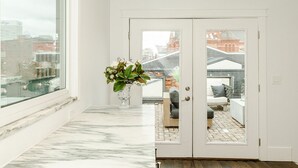 Un intérieur moderne avec un sol en marbre, une porte blanche donnant sur un espace extérieur et une vue sur le paysage urbain à travers une grande fenêtre.