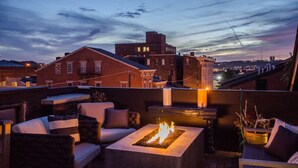 Une terrasse sur le toit, dotée d’un espace extérieur aménagé et d’un foyer, offrant une vue sur le paysage urbain au crépuscule.