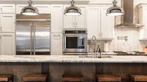 Une cuisine moderne dotée d’appareils électroménagers en acier inoxydable, de meubles blancs et de tabourets de bar.