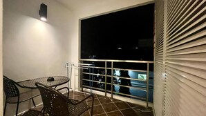A balcony with a table and chairs, a view of the night sky, and a window with blinds. - 6-15 - 1 Bdr Condo With Balcony and Shared Pool (Patong)