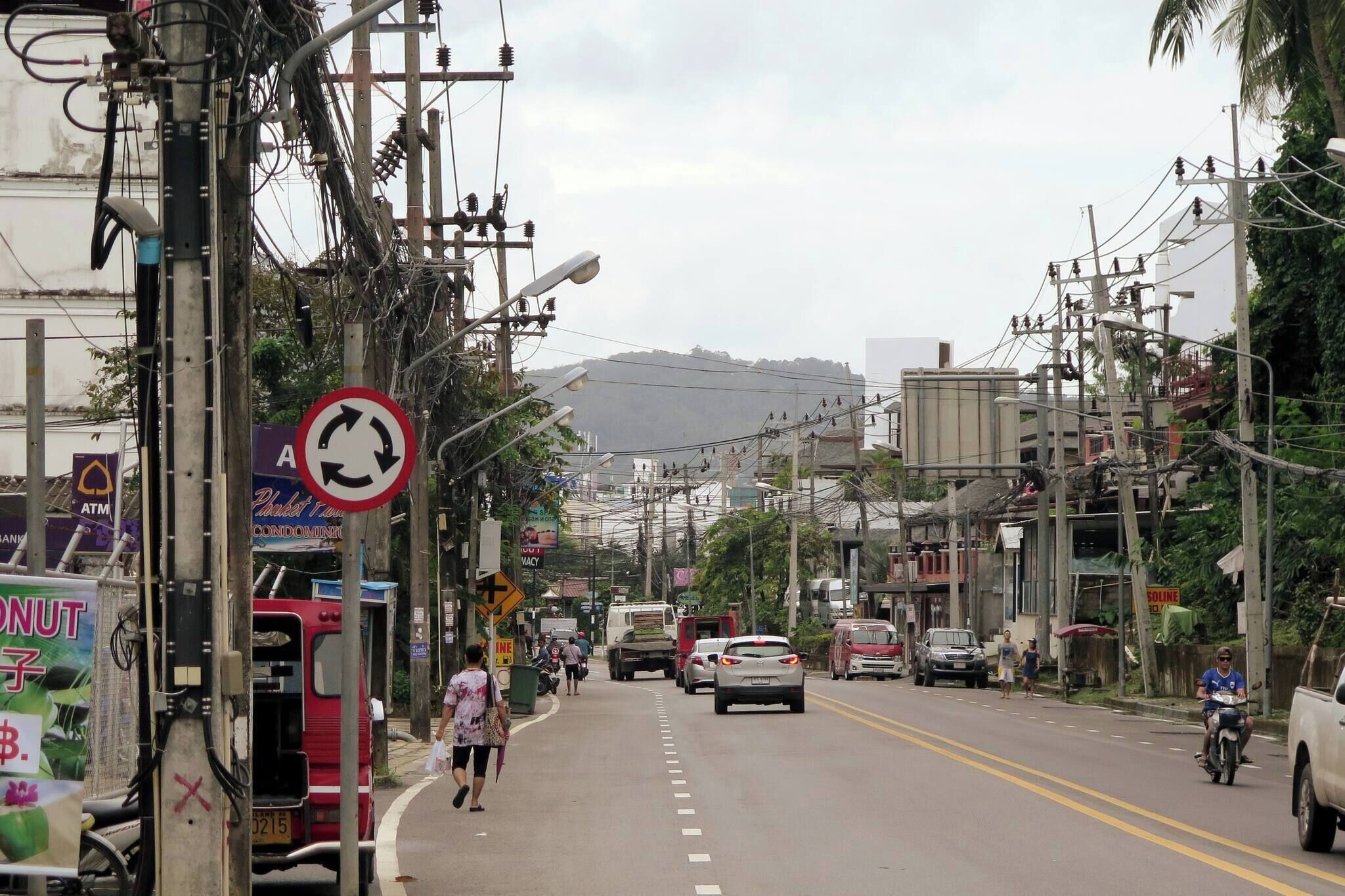 Eine Straße mit Fahrzeugen, Fußgängern und Strommasten.