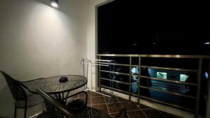 A balcony with a metal railing, a round table with chairs, and a view of a cityscape at night.