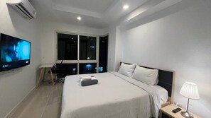 A modern hotel room with a large bed, a TV mounted on the wall, a desk with a lamp, and a window providing a view of the night sky.