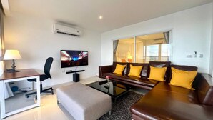 A modern living room with a sofa, a coffee table, a TV, and an air conditioning unit. - A11 - 2 Bdr Condo, Stunning Sea View, Karon Beach (Karon)