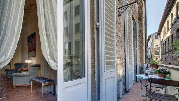 A narrow outdoor corridor with a white door, a small table with a plant, and a chair. - Piazza Salvemini Elegant (Florence)