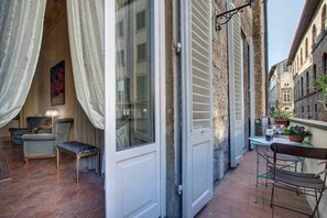 Un estrecho pasillo exterior con una puerta blanca, una pequeña mesa con una planta y una silla.