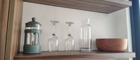 Een houten plank met een groene lantaarn, drie wijnglazen en een heldere fles.