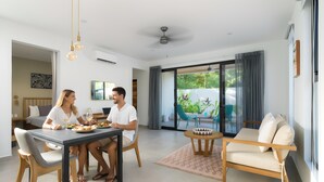 Una sala de estar moderna con una mesa de comedor, dos personas cenando, un sofá y vistas al exterior.